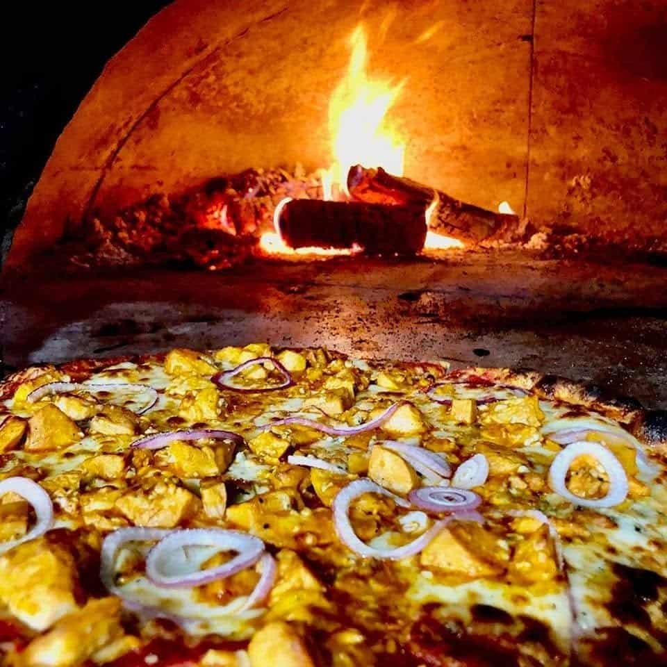 A pizza cooking in the wood-fired oven at 17 Cherry Plain Square, flames burning at the back of the oven